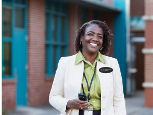 black woman working at a school wearing oval name tag on her white blazer
